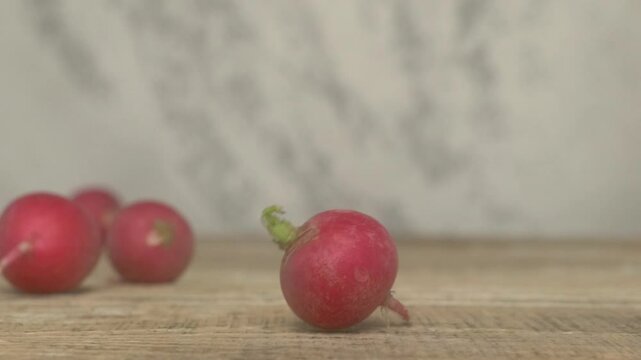 Fresh, vibrant red radishes tumble pleasantly and noisily onto a rustic wooden surface