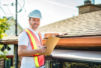 man with hard hat standing on steps inspecting house roof