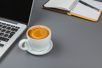 Cup of coffee on desk with laptop and open notebook in office setting