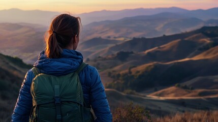 Woman gazing at layered mountain vistas at sunrise, bathed in a blend of orange and purple hues, conveying peace and inspiration.