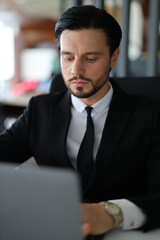 Fototapeta premium A man in a suit is sitting at a desk with a laptop in front of him. He is wearing a tie and he is focused on his work