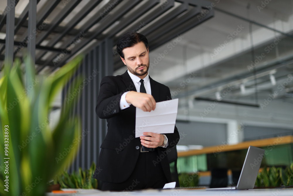 Poster a man in a suit is reading a piece of paper. he is looking at the paper with a serious expression on
