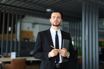 A man in a suit holding a pencil and a clipboard. He looks serious and focused. Concept of...