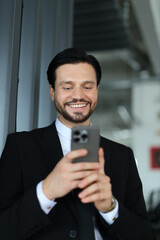 A man in a suit is smiling while looking at his cell phone. He is wearing a tie and he is in a professional setting