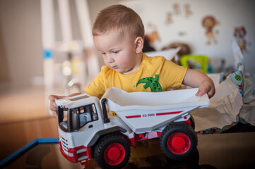 Toddler plays with a large toy dump truck in a bright, colorful indoor play area during the morning...