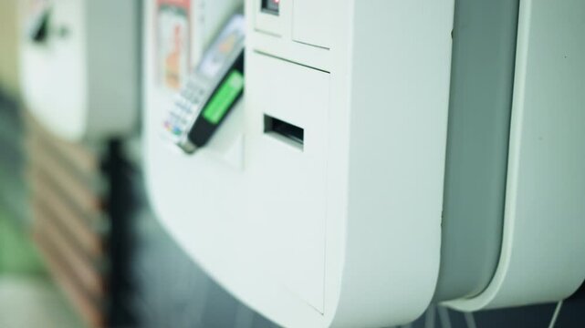 Lady's hand retrieving receipt from white ATM machine after making a transaction, wearing wrist chain, other ATM machines are slightly visible in background, while standing in a well-lit space