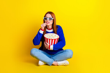 Photo of woman in blue stylish pullover jeans sitting alone eating popcorn and scared watching movie isolated on yellow color background