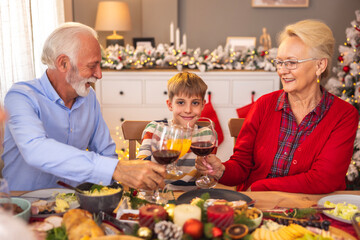 Boy making a toast with grandparents while having family Christmas dinner at home