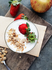 Yogurt with granola and strawberry in glass bowl on board and gray background