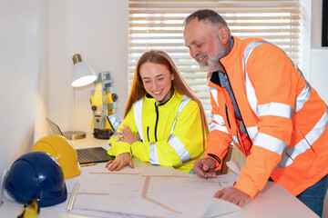Collaboration Between Young Engineer and Mentor Over Blueprints in Bright Office Setting