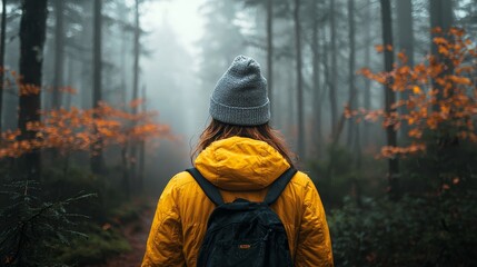 Obraz premium Woman in a yellow jacket exploring a misty forest with autumn orange leaves, evoking a mysterious and serene atmosphere.