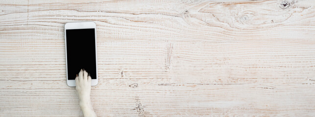 Dog paw holding cell phone with empty black screen. Wooden background table. Long horizontal background with copy space template © Iryna&Maya