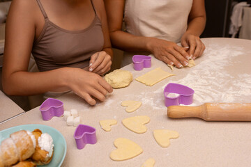 Cookies Baking Kitchen: Two women are making heart-shaped cookies in a kitchen, using cookie cutters and rolling dough on a floured surface.
