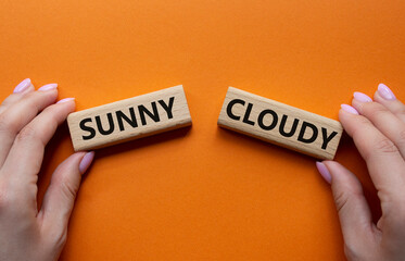 Sunny or Cloudy symbol. Concept word Sunny or Cloudy on wooden blocks. Businessman hand. Beautiful orange background. Business and Sunny or Cloudy concept. Copy space