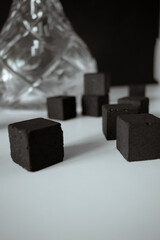 Hookah with coals on white surface on black background. Black charcoal cubes lay randomly. Space for text. Soft focus.