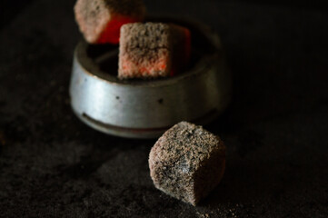 Hookah bowl with foil and embers, saucer, and tongs on a black background. White smoke. Hot red...