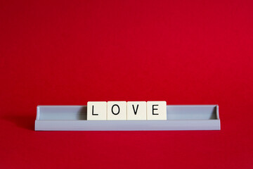 Love word spelt out in square tiles in a grey letter holder against a red background 