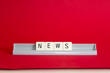News written in alphabet tiles in letter holder against a paper red background with edge showing 