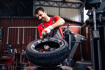Skilful worker mounting new car tire on the wheel. Changing tires for winter season.