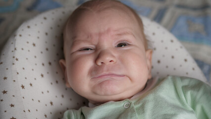 Close-up of face of newborn baby toddler lying in crib and crying loudly for food. Hysterics before going to bed, demands a mother.