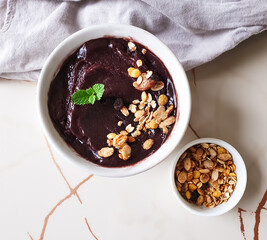 Iced açaí with granola and mint in white bowl and  marbled background with space for text