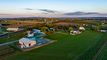 An expansive aerial view captures the serene beauty of rural Pennsylvania at sunset, showcasing farmland, trees, and residential areas. The vibrant landscape reflects the tranquility of country life. © Greg Kelton