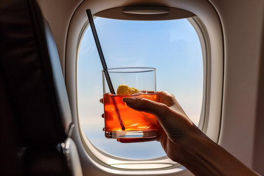 Close-up of a woman's hand holding a glass of Aperol Spritz cocktail while flying on board an airplane in business class
