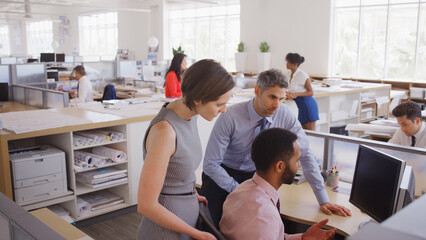 Multi-Cultural Business Team Meeting Around Desk In Modern Open Plan Architects Office Together