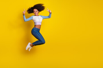 Full body photo of attractive young woman jump show v-sign dressed stylish blue clothes isolated on yellow color background