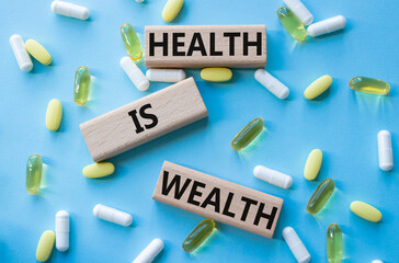 Health is Wealth symbol. Concept word Health is Wealth on wooden blocks. Beautiful blue background with pills. Medicine and Health is Wealth concept. Copy space