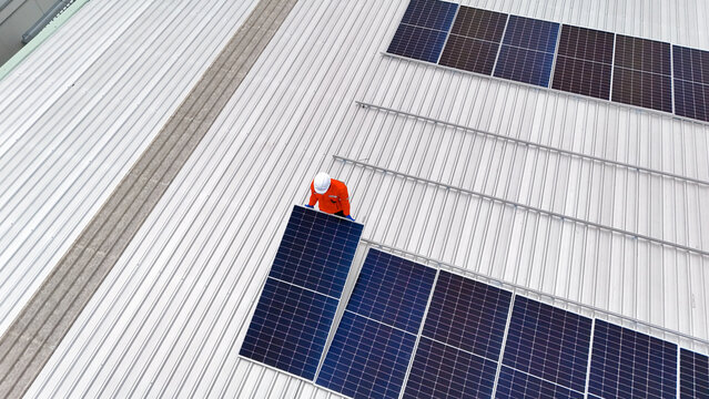 Builder mounting photovoltaic solar modules on roof of house. Back view of man engineer in helmet installing solar panel system outdoors. Concept of alternative and renewable energy.