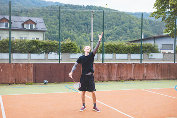 Badminton player stands ready to serve on an outdoor court, holding a racket and shuttlecock....