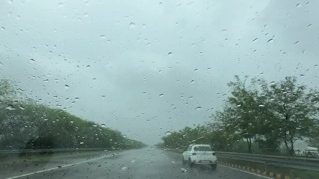 Heavy raining during monsoon and droplets textured on glass of moving car in the highway roads.