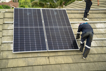 Builder mounting photovoltaic solar modules on roof of house. Back view of man engineer in helmet...