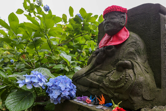 Stone Jizo statue resting with origami cranes and blue hydrangeas