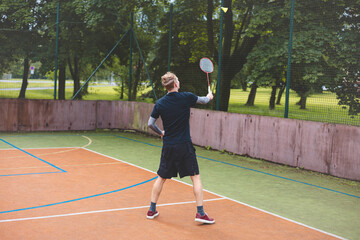 Badminton player focuses on the shuttlecock mid-air during a match on an outdoor court. With his...