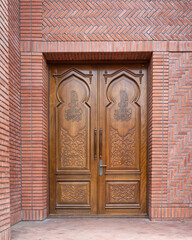 Elaborate wooden doors showcase detailed carvings, standing prominently in a brick backdrop, highlighting the craftsmanship and design