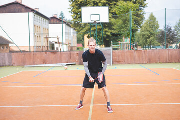Obraz premium Badminton player focuses on the shuttlecock mid-air during a match on an outdoor court. With his racket raised, he prepares for the next shot, surrounded by an urban and scenic background