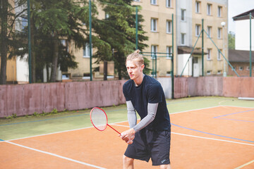 Badminton player focuses on the shuttlecock mid-air during a match on an outdoor court. With his...