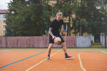 Basketball player controls and dribble the ball during a casual game on an outdoor court, bending down in focus. The court is surrounded by trees and nature, giving a peaceful and athletic atmosphere