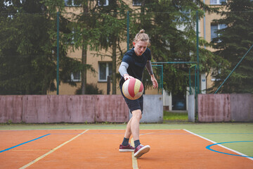 Basketball player controls and dribble the ball during a casual game on an outdoor court, bending down in focus. The court is surrounded by trees and nature, giving a peaceful and athletic atmosphere
