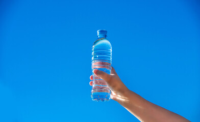 A girl holds a bottle of drinking water in her hand against a blue sky background
