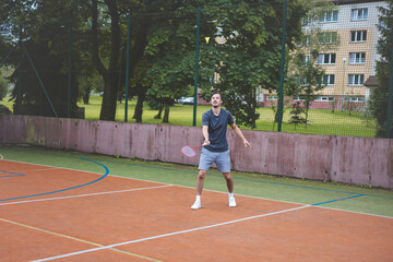Badminton player focuses on the shuttlecock mid-air during a match on an outdoor court. With his...