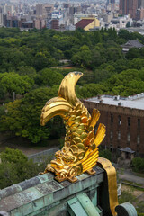 Golden shachihoko fish ornament on Osaka Castle roof overlooking city