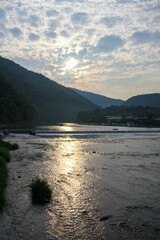 Sun reflecting on rippled river water near mountains at sunset
