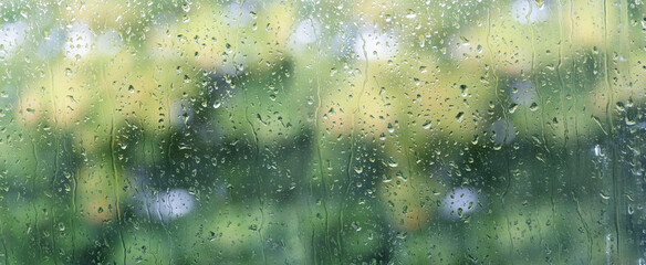 Rain drops on glass transparent window with green blurred background of garden. Drops run down. Widescreen image