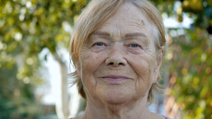 Portrait nice alone senior old age wrinkled caucasian female looking at camera. Happy mature elderly grandmother in green garden park outdoor summer day. Senior 80s pensioner resting