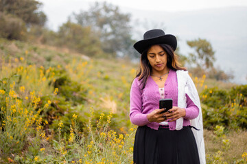 Foto de una feliz y bonita campesina con un sombrero hablando por un teléfono celular en los Andes peruanos. Mujer usando teléfono móvil