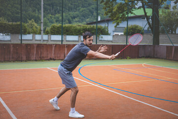 Badminton player focuses on the shuttlecock mid-air during a match on an outdoor court. With his...