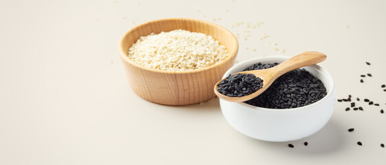 Black sesame in white bowl with wood spoon and white sesame on beige background